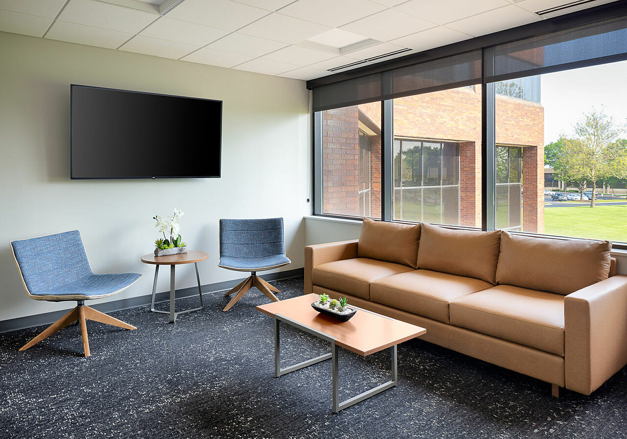 Watco living/meeting room with caramel leather sofa and coffee table and two modern side chairs with blue textured upholstery. Orchids on table under TV