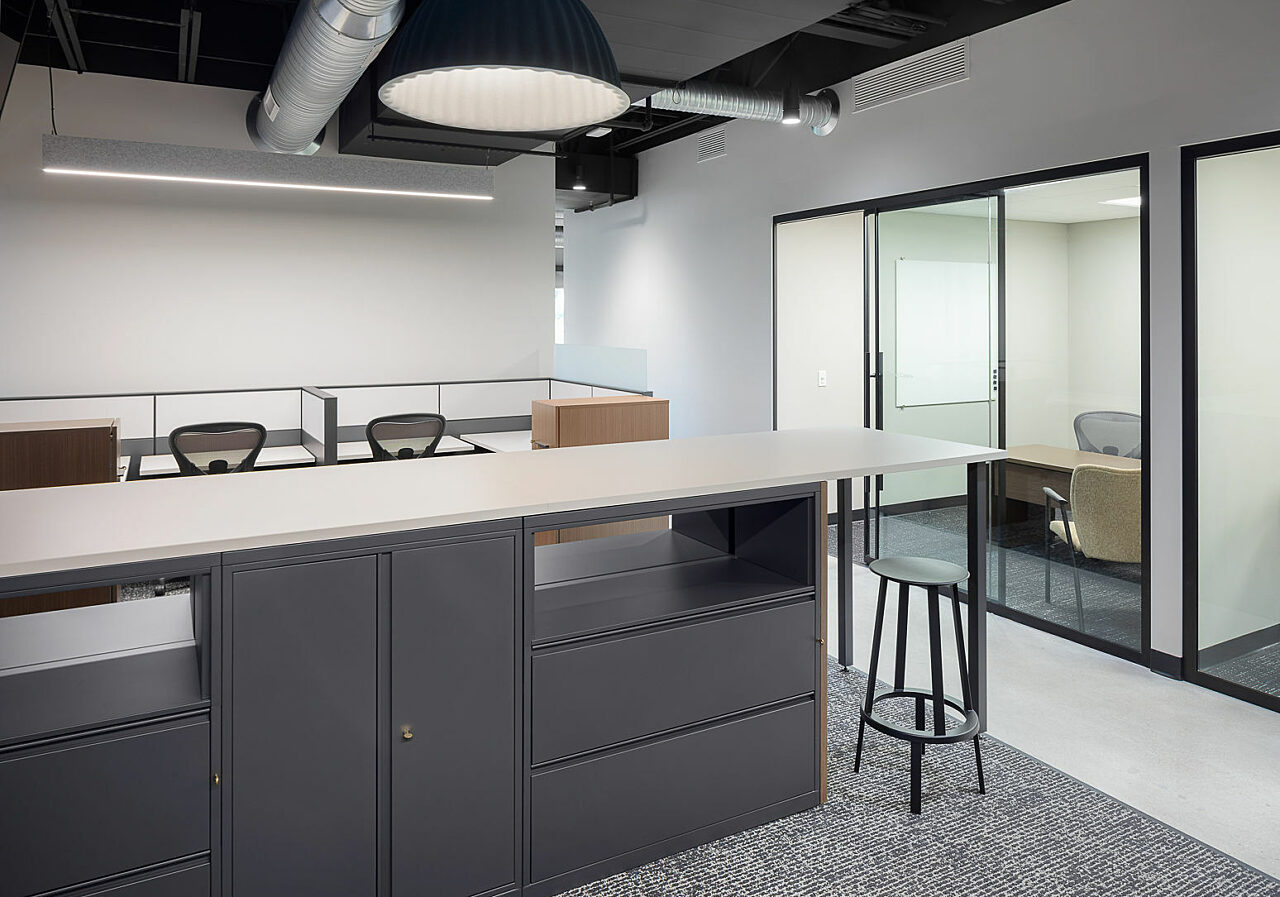 Meridian storage unit w/ built in collaborative area and stools are surrounded by multiple workstations. View of private office in background.