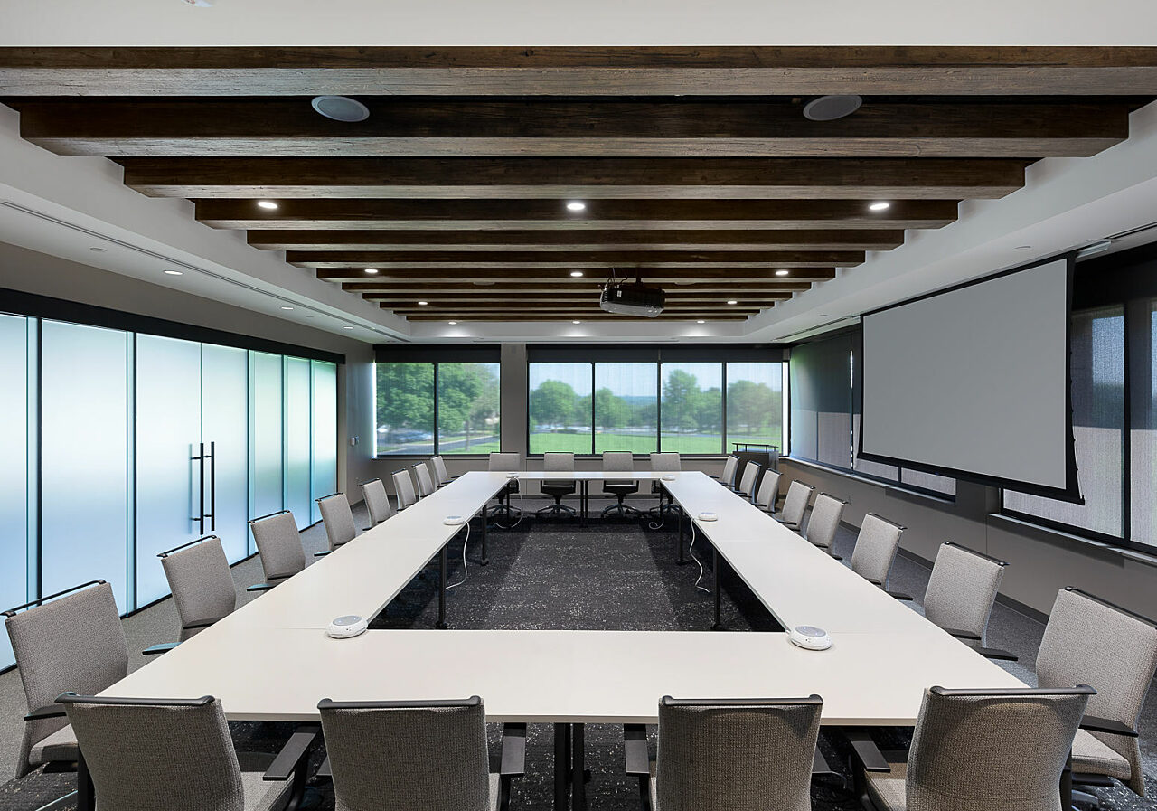 Watco Training Room w/ tables arranged in large rectangle and grey chairs around. Large screen on wall, frosted glass wall separates room from another room