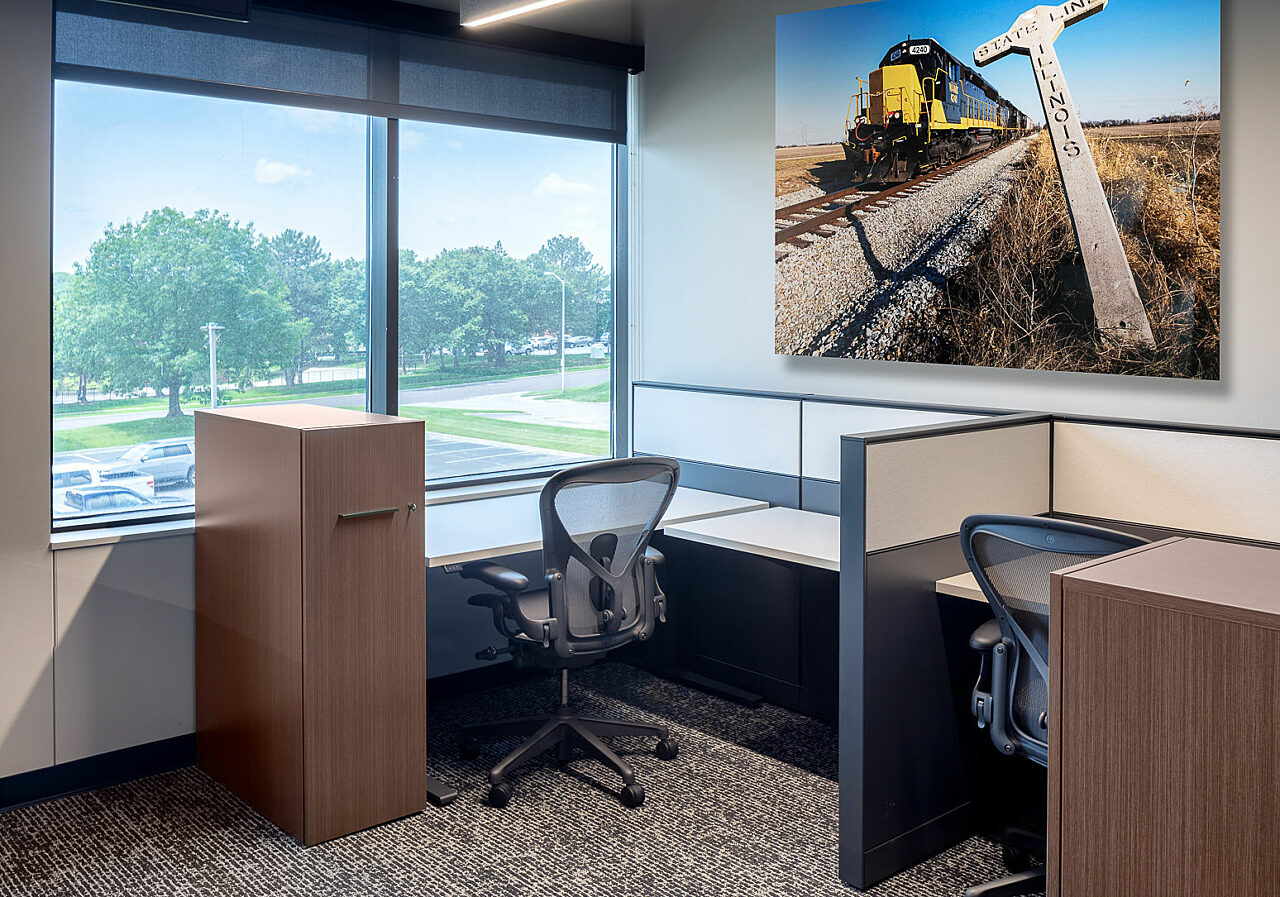 Two Watco work stations with locker storage, Aeron chairs and large railroad art on wall. Next to a window.