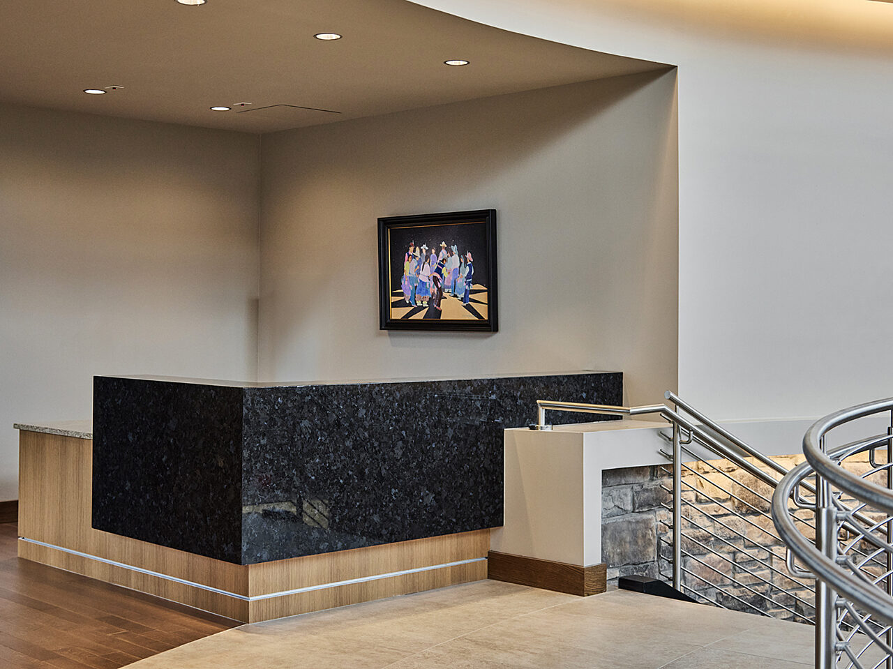 Reception desk at top of staircase. Wood with a black L-shaped marble or granite panel. Painting hangs on wall next to desk.