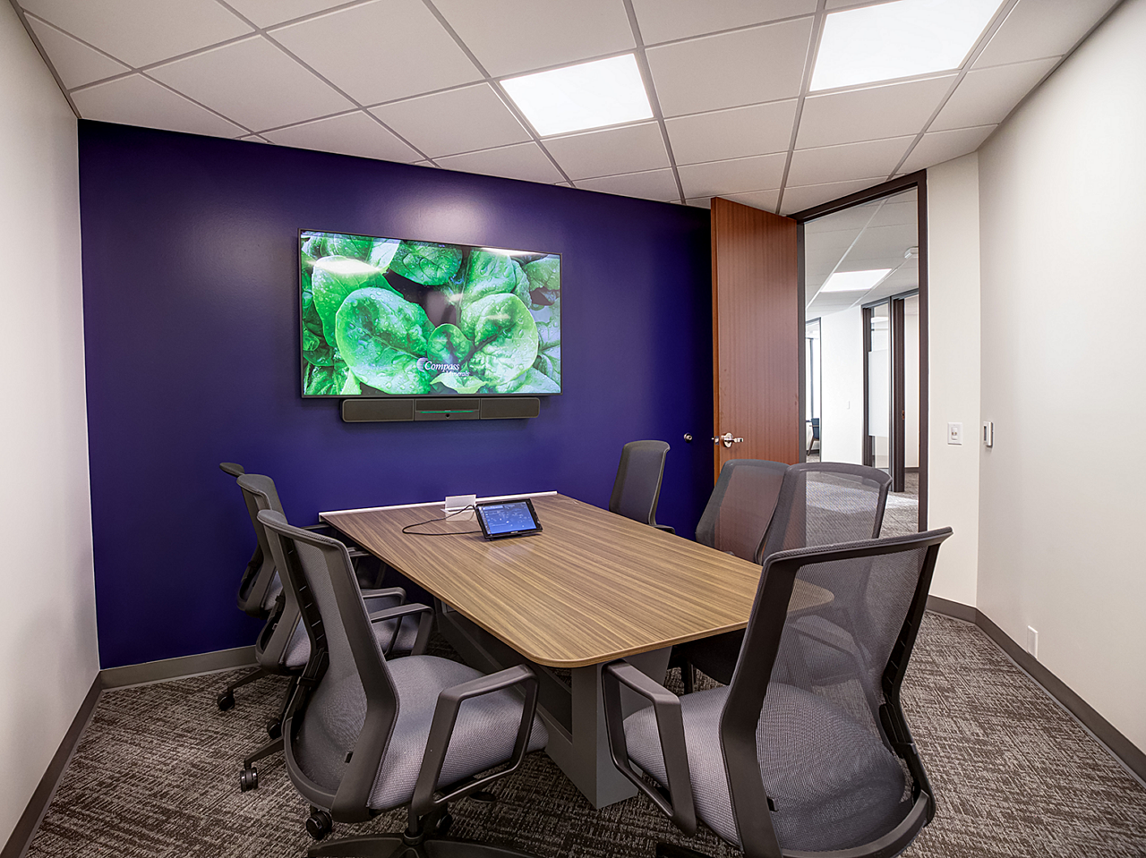 Compass Minerals-Small meeting room w/ dark blue wall and mounted tv.  Table just from the wall with triangular base and is surrounded w/ mesh back chairs