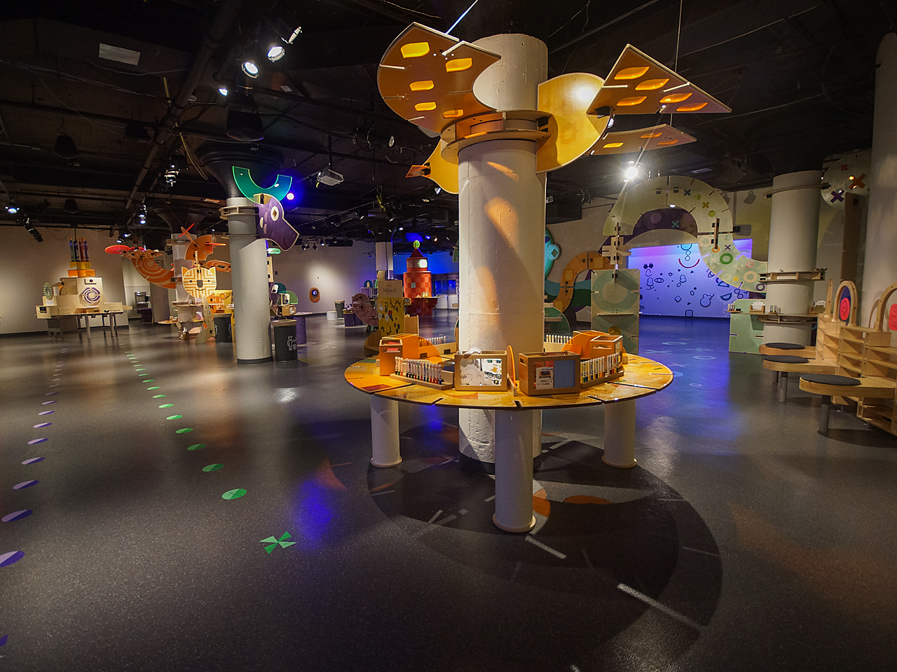 Long view of Hallmark Kaleidoscope exhibits throughout a wide open area, with colorful displays with art materials that are spotlighted.