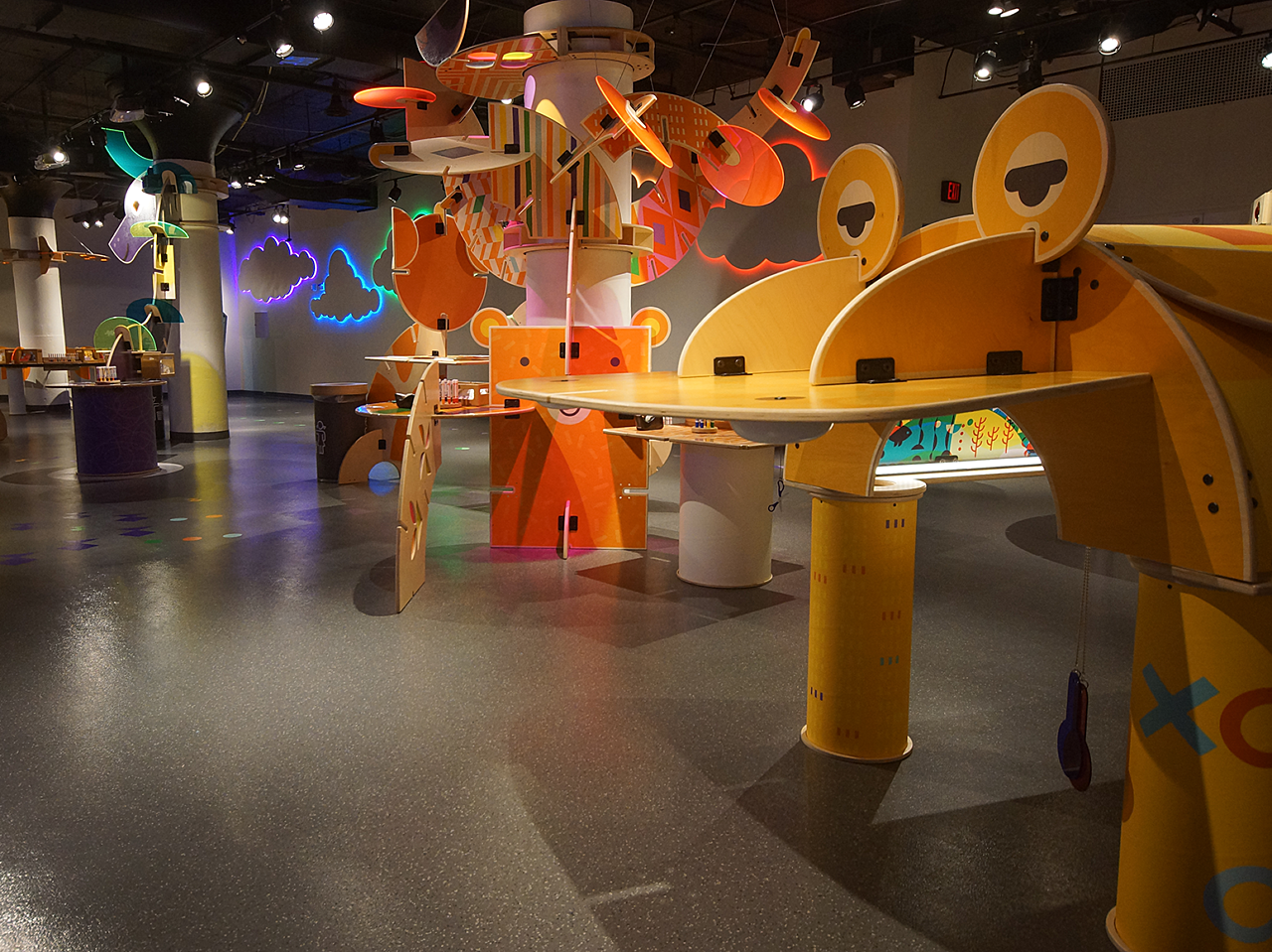 Hallmark Kaleidoscope art stations featuring a giant yellow frog, and a tall mobile-like exhibit with orange slatted pieces flowing off of it.