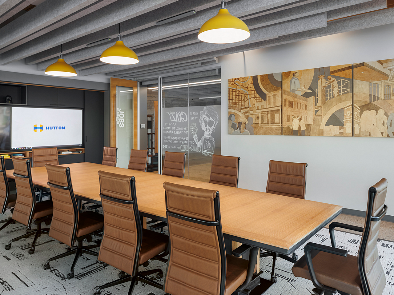 Hutton Construction Conference Room with large table and brown leather high-backed chairs. Wall contains artwork in brown/grey/beige. Yellow drop lights.