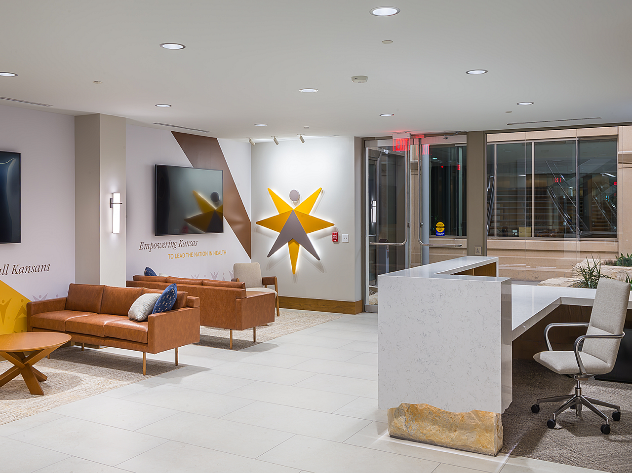 Reception area with brown leather couches and coffee tables, stone reception desk, white wheeled task chair. Gold/orange/brown star design on wall