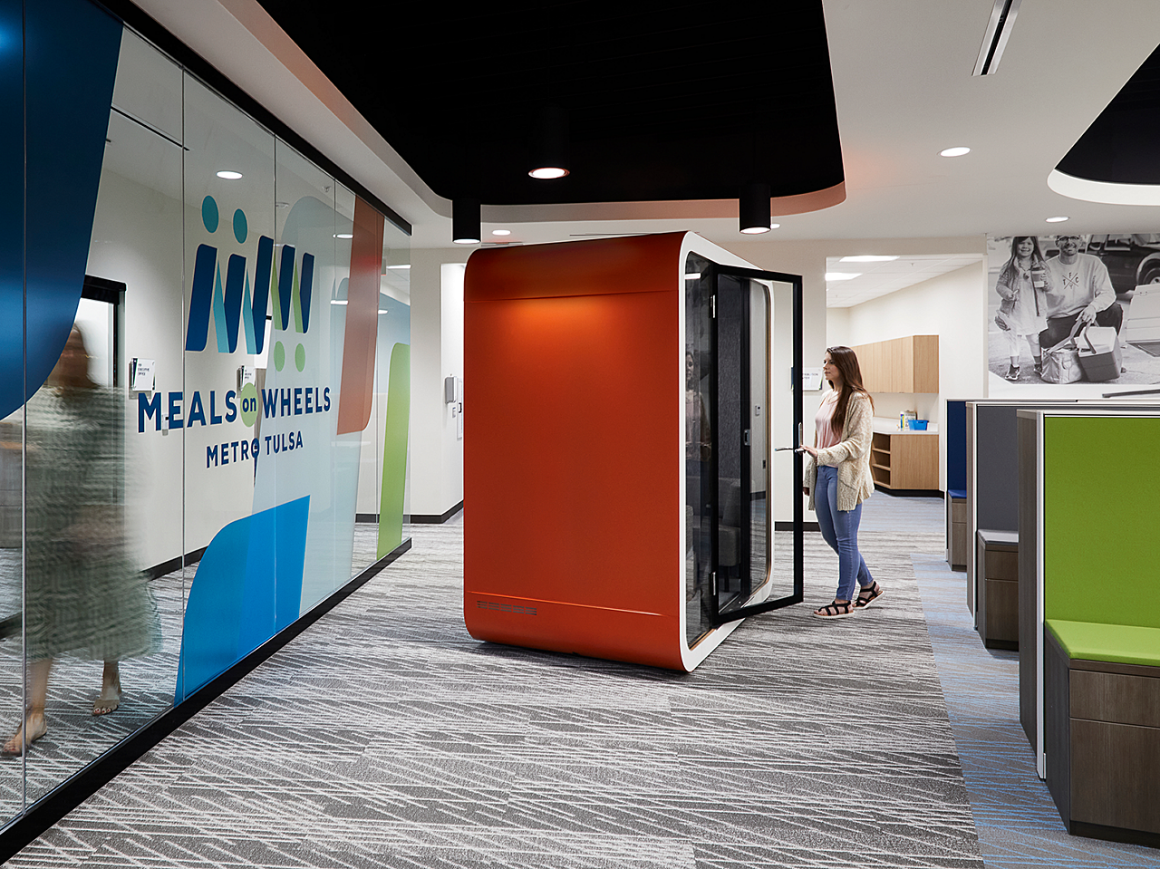 A female employee gets ready to enter a red and white, soundproof, acoustical work pod, which is located just outside a bank of workstations.