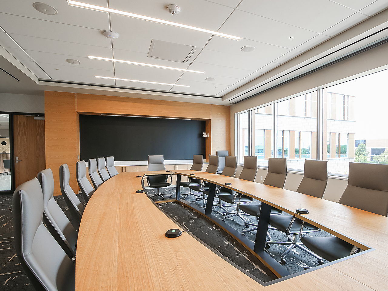 WSU Woolsey Hall board room.  Unique shaped wooden conference table with interior removed. High Back grey conference chairs surround the table.