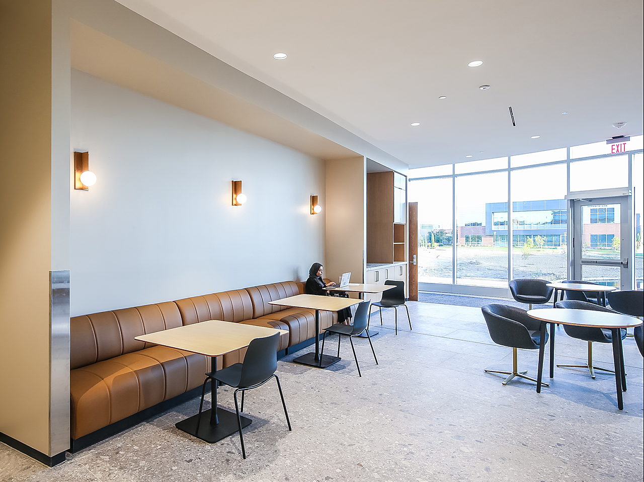 WSU's Woolsey Hall-A cafe area with brown leather banquette and cafe seating and blue upholstered chairs.  A female student uses a laptop at a far table.