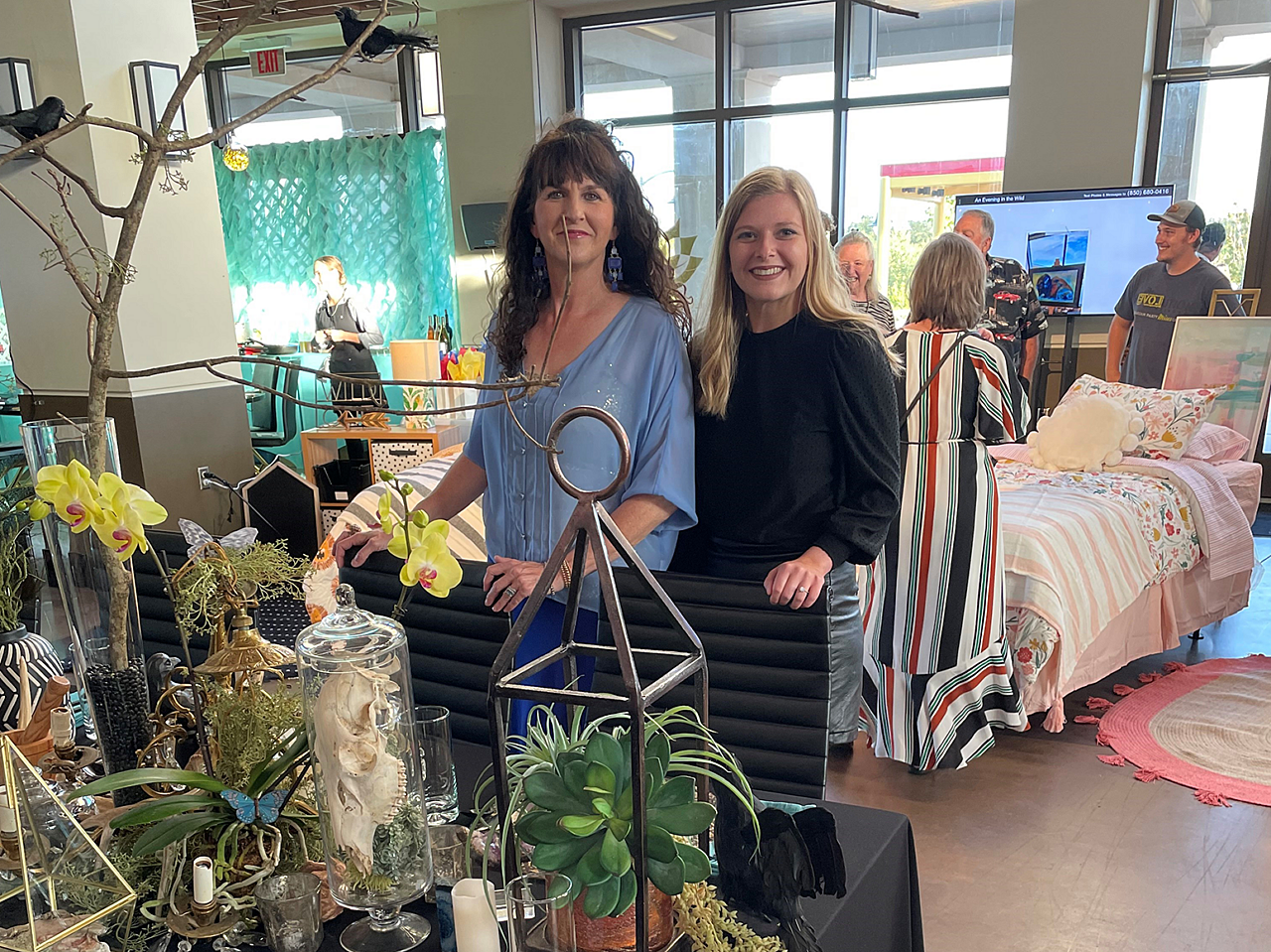 Two John A. Marshall Co. designers pose at table they designed, while attendees look at different child-sized beds in the background.