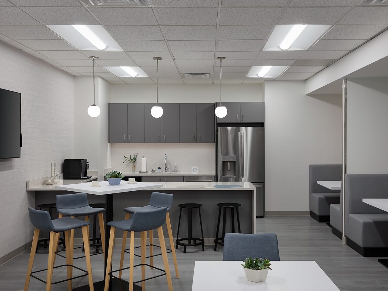 Kitchen/cafe area with high- and low-top tables with blue stools/chairs. Two booths with walls allow for private conversations. Black stools at counter.