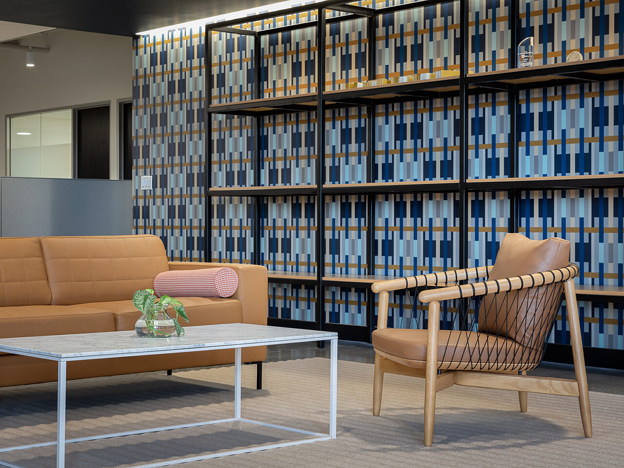 Camel colored sofa and Geiger Crosshatch chair with coffee table in front of a wall with vivid wallpaper design of dark/light blues and beige rectangles