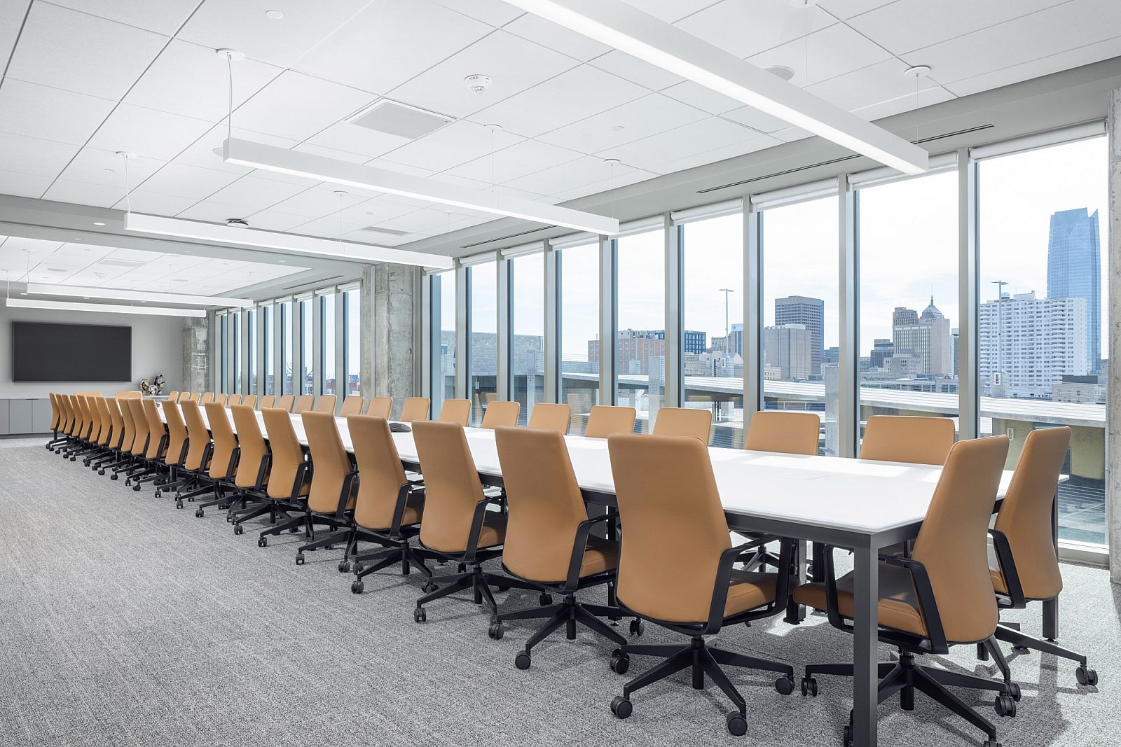Large window-lined room with long conference table with 44+ camel leather high back chairs