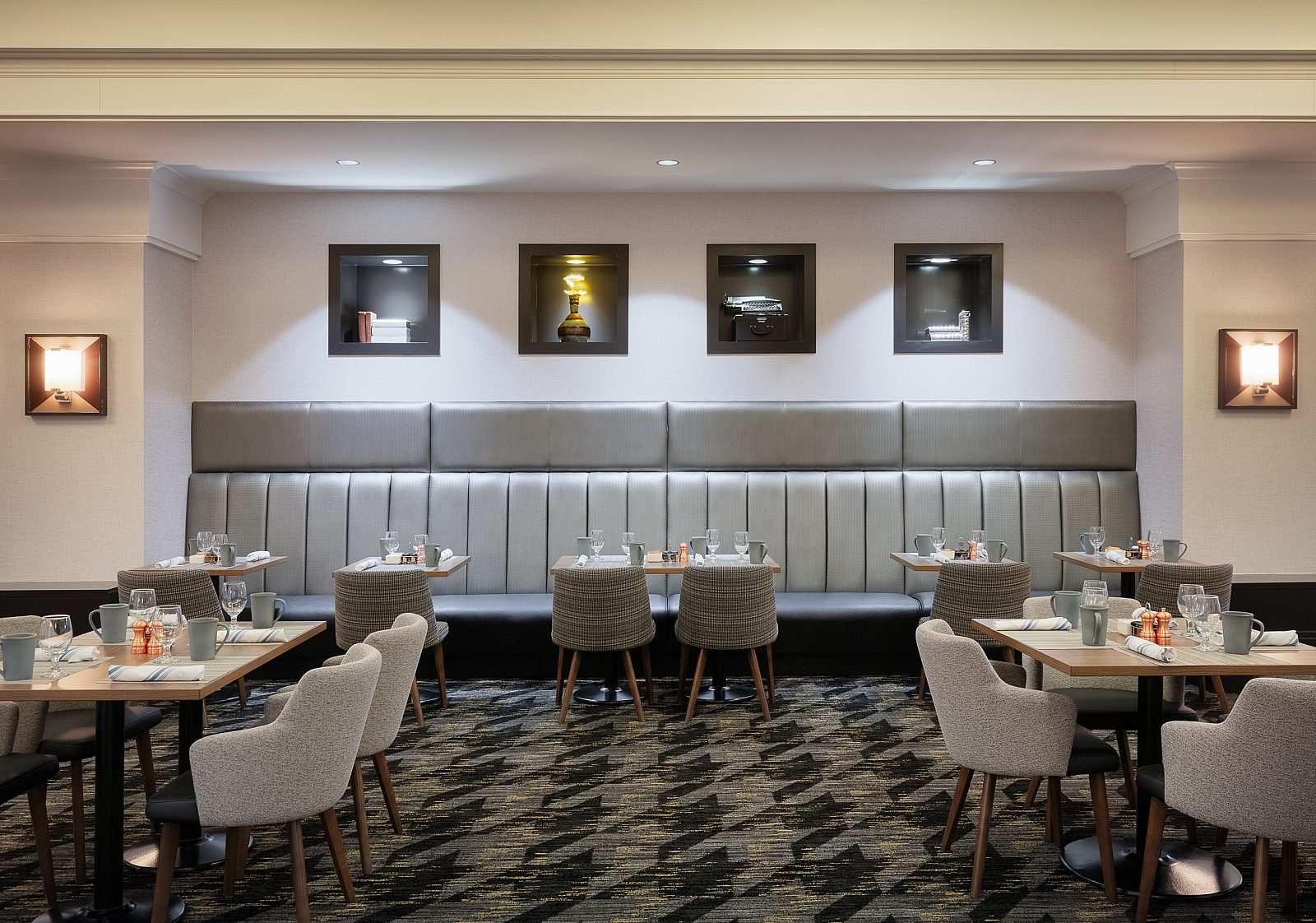 Sheraton Overland Park dining room. Silver/grey banquette seating with grey cafe tables with wooden legs. Matching carpet with a bold repeated graphic
