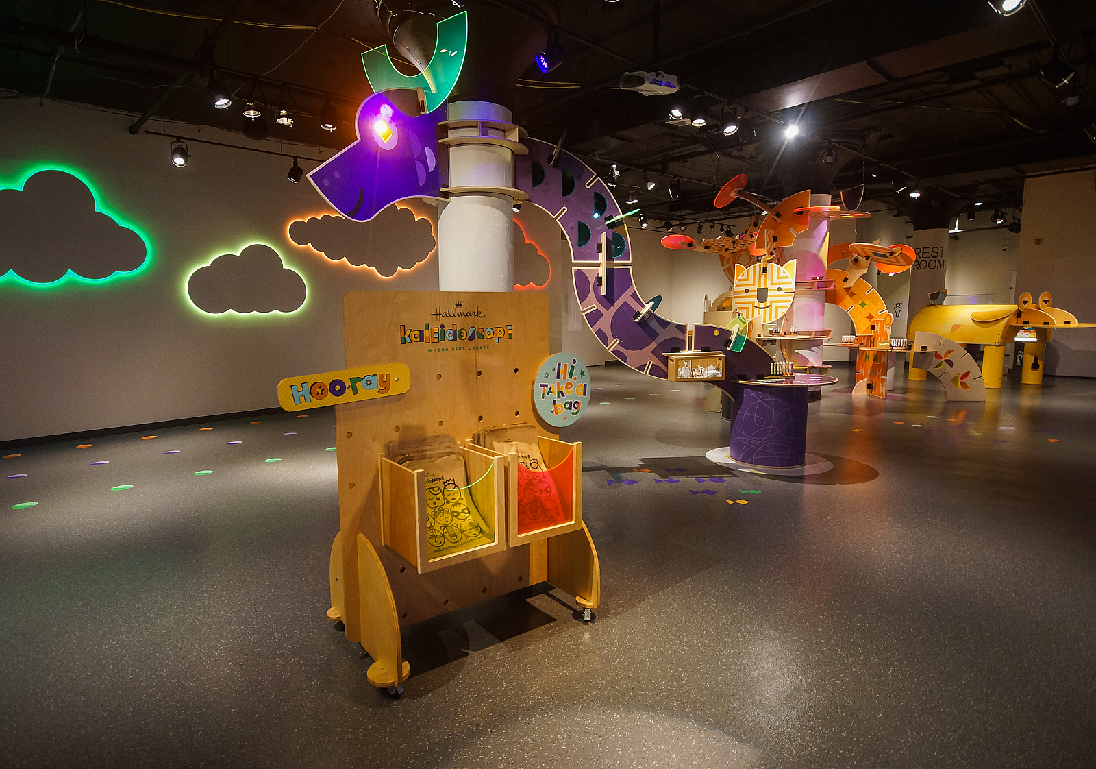 Hallmark Kaleidoscope logoed cart with a long, brigtly lit dragon display and lit up clouds on the walls. Several art stations can be seen throughout rom