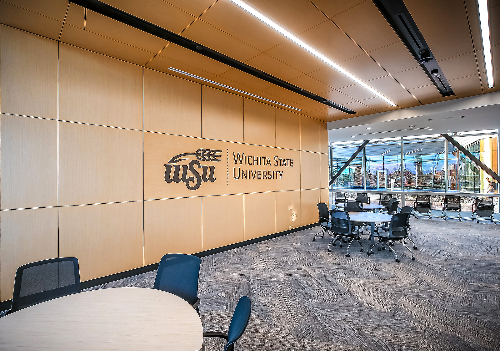 WSU Woolsey Hall-Wooden wall with college logo and round tables and rolling conference chairs give students several options to study and socialize.