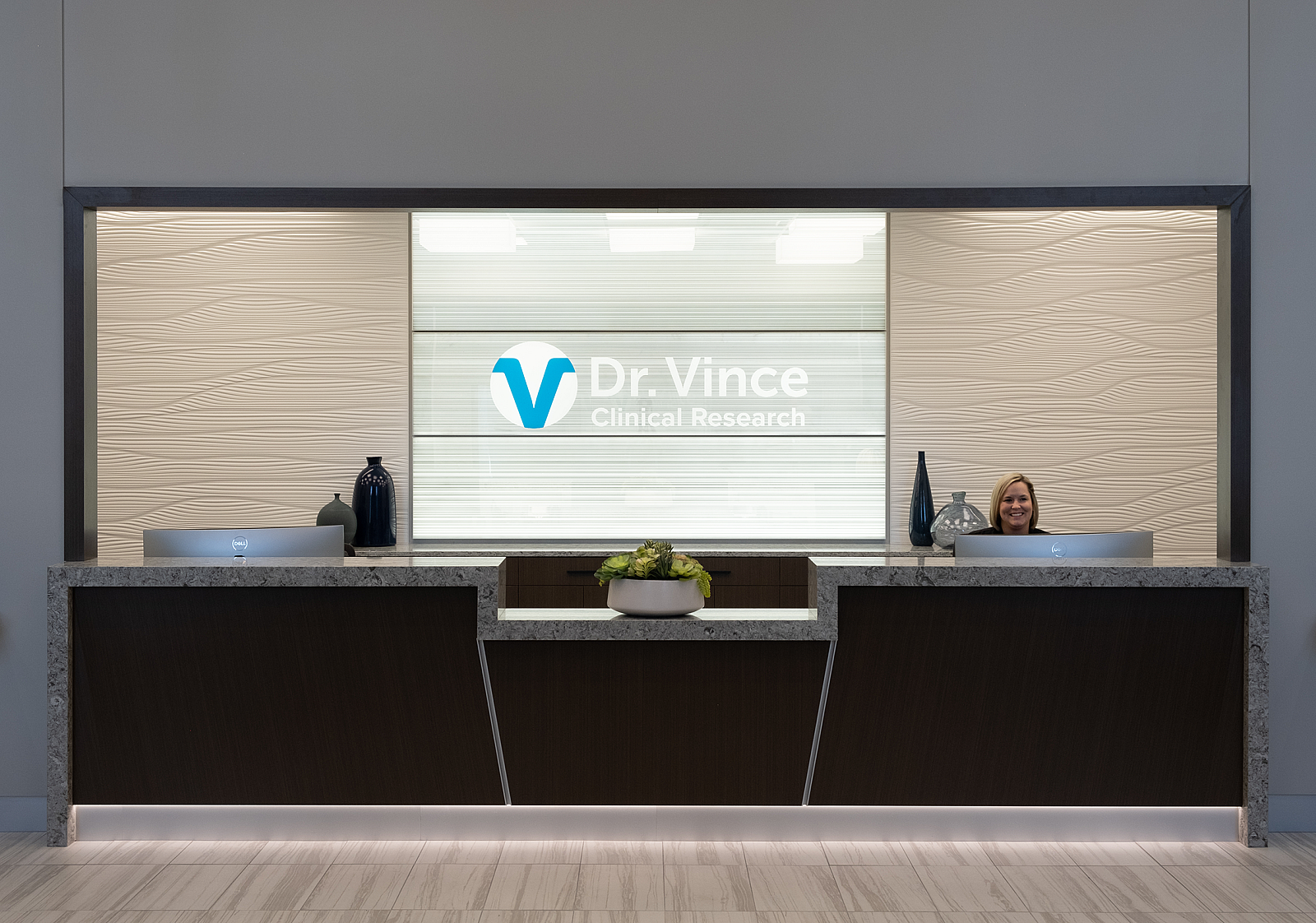 Dr. Vince Clinical Research reception area with logo on back wall, a smiling receptionist and a black counter with black marble waterfall trim