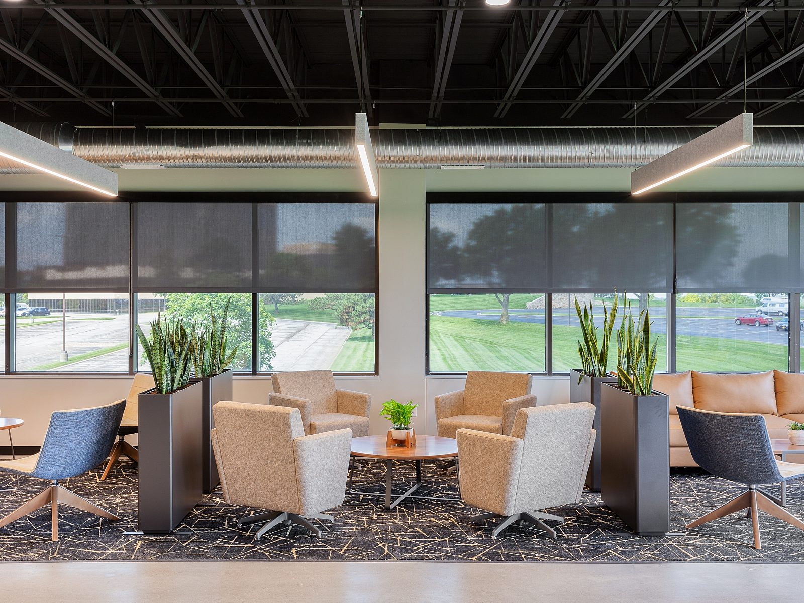 Long Watco seating area - mix of neugral/wood lounge chairs, couches, tables. Each area divided by planters with tall green plants. Grey patterned rug
