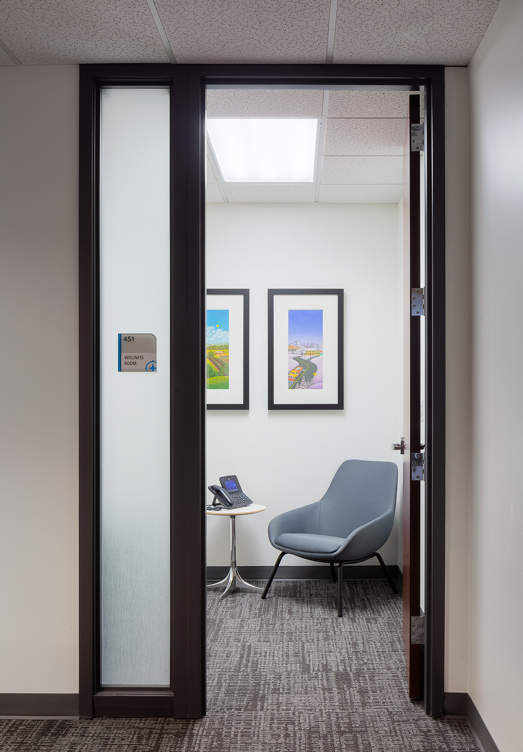 Compass Minerals Employee Wellness room featuring a small chair with office phone and blue/grey lounge chair. Enclosed with frosted glass and closing door.