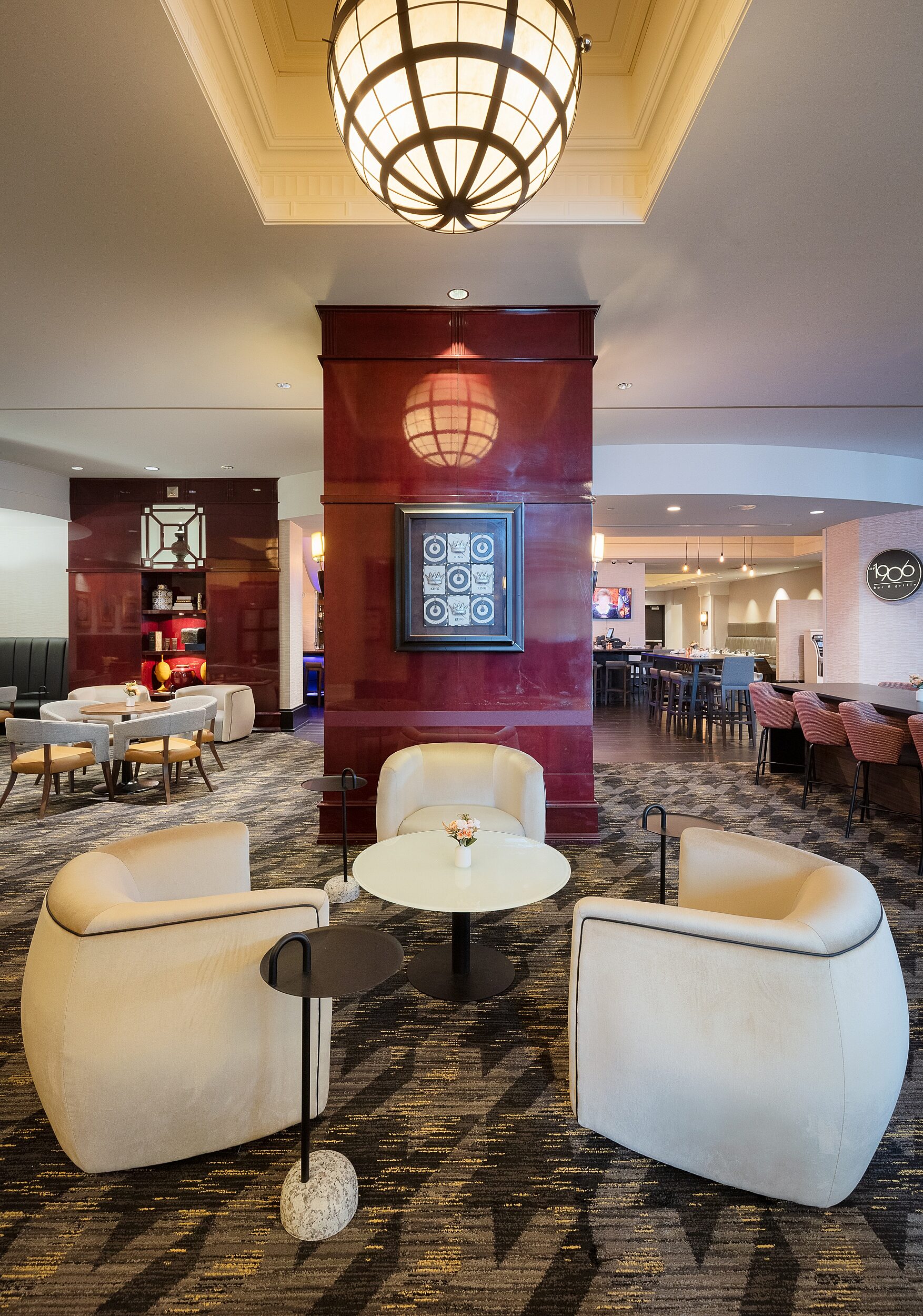 Lounge seating ara. White sleek curved chairs around white pedestal coffee table. Various seating types around. Partial burgandy walls with artwork.