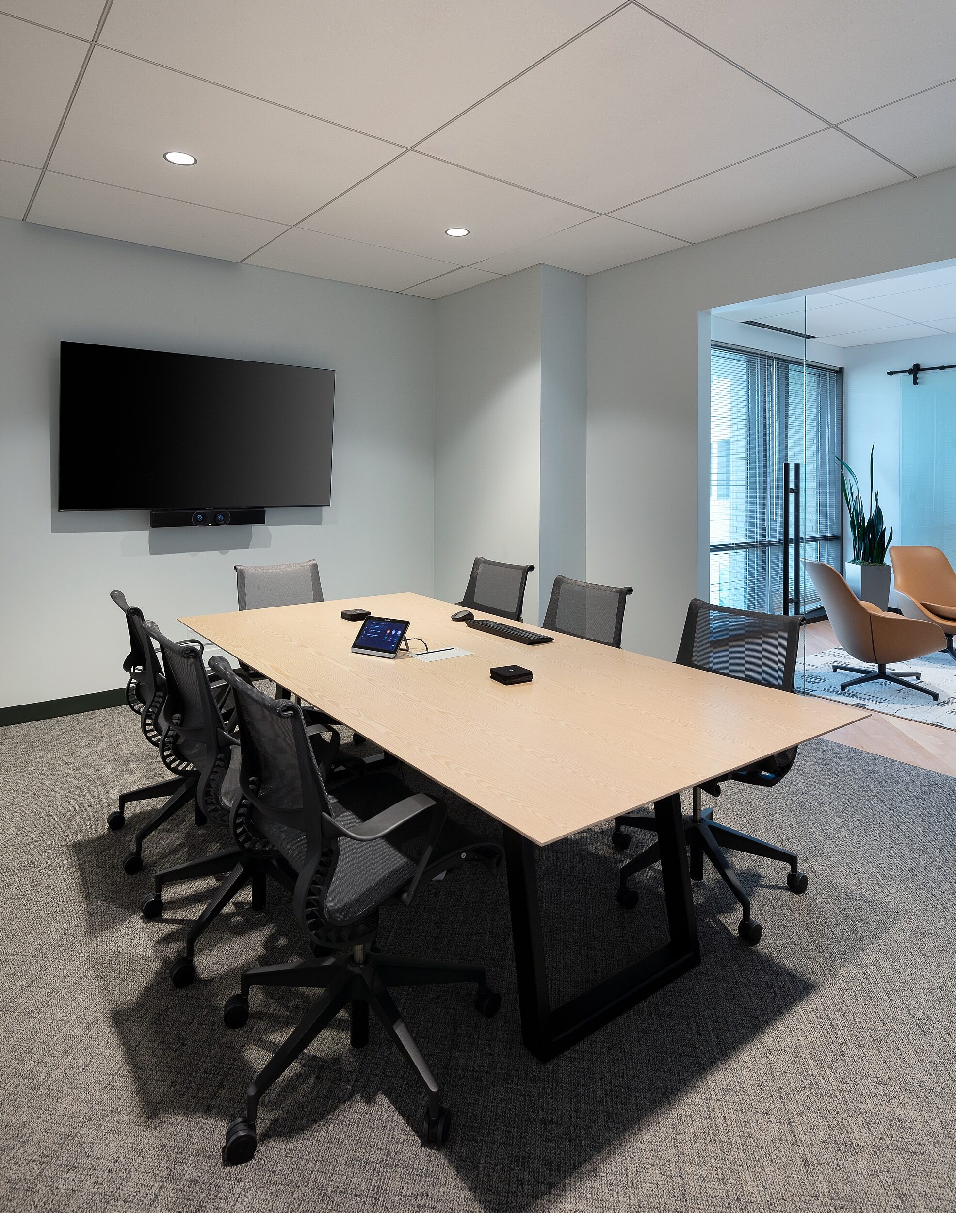 DRI small conference room with TV on one wall. Lounge area with tan leather seating can be seen in distance. Sliding glass doors.
