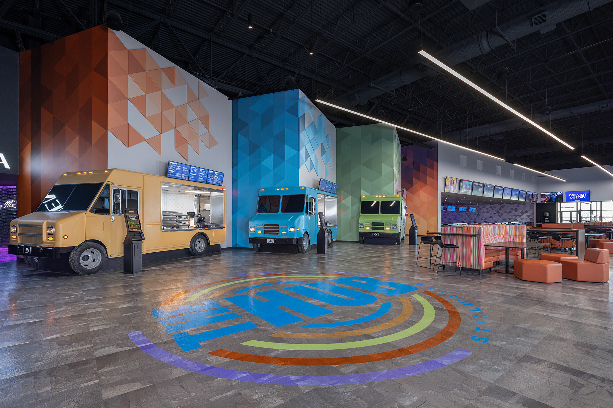 Dining at The Hub in Stillwater, OK. Orange, blue and green stationary food trucks serve as individual cafes. Colorful seating options are beside them.