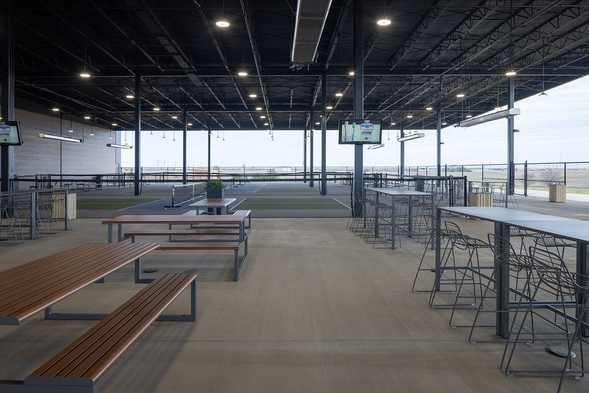 Outdoor sports bar seating area with picnic and high-top seating. Pickleball courts in the background. Part of The Hub, owned by the Tonkawa Tribe of OK.
