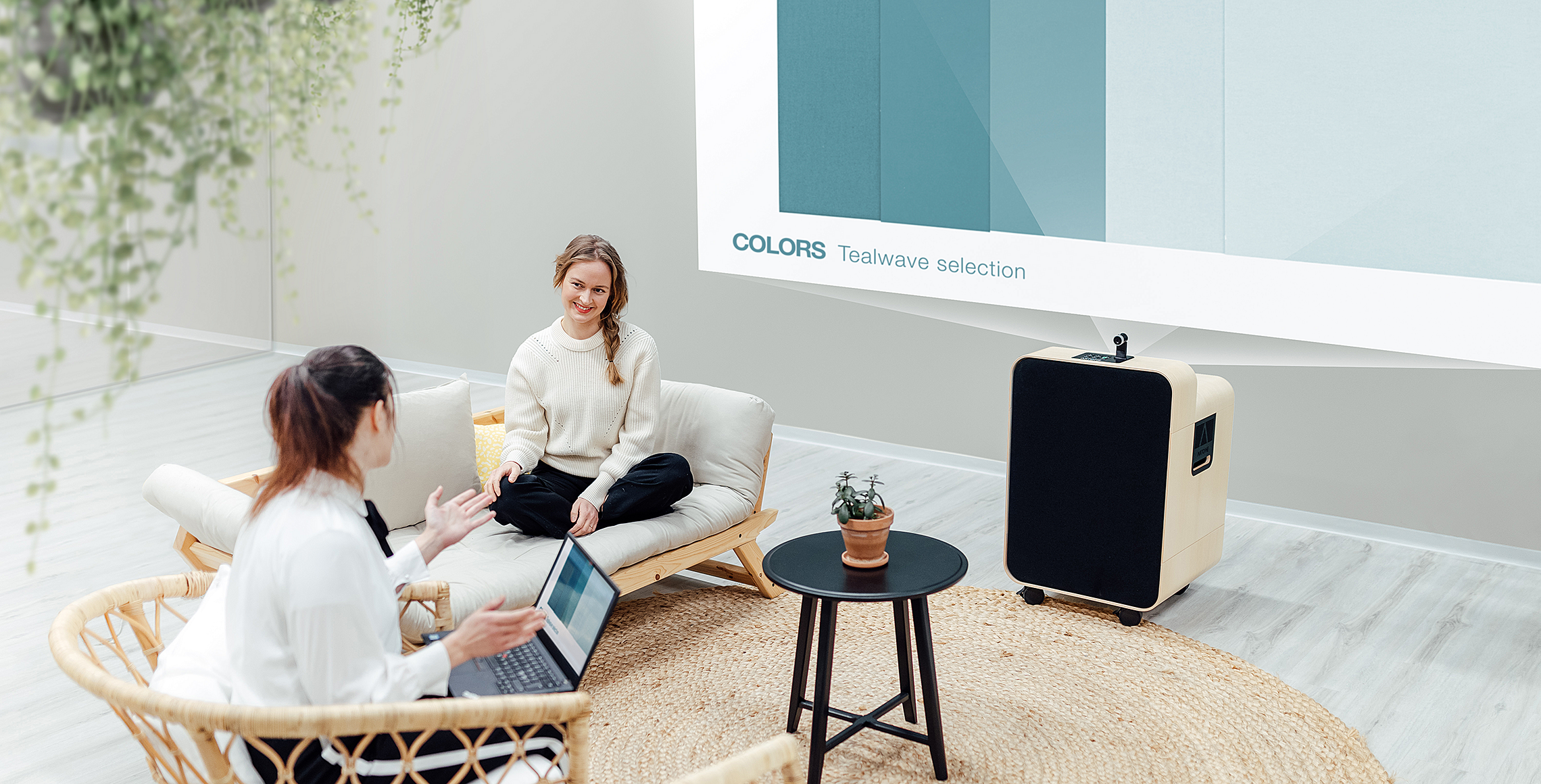 Two women in scandinavian style furniture discuss a project with the M10 projecting the project on the wall of the space.