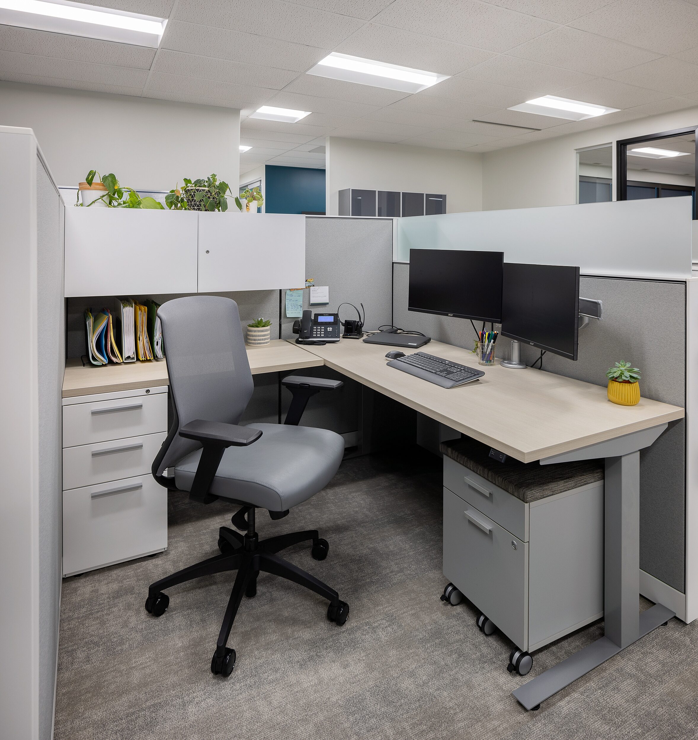 Workstation with pale desktop and grey tackboard, three drawers and 2side by side upper cabinets, mobile pedestal storage underneath, frosted glass  pane