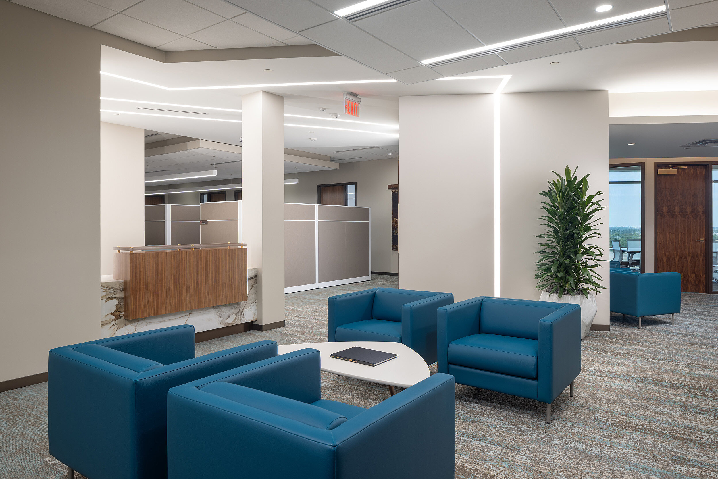 Lounge seating area feature blue u-shaped upholstered chair groupings with triangular shaped tables.