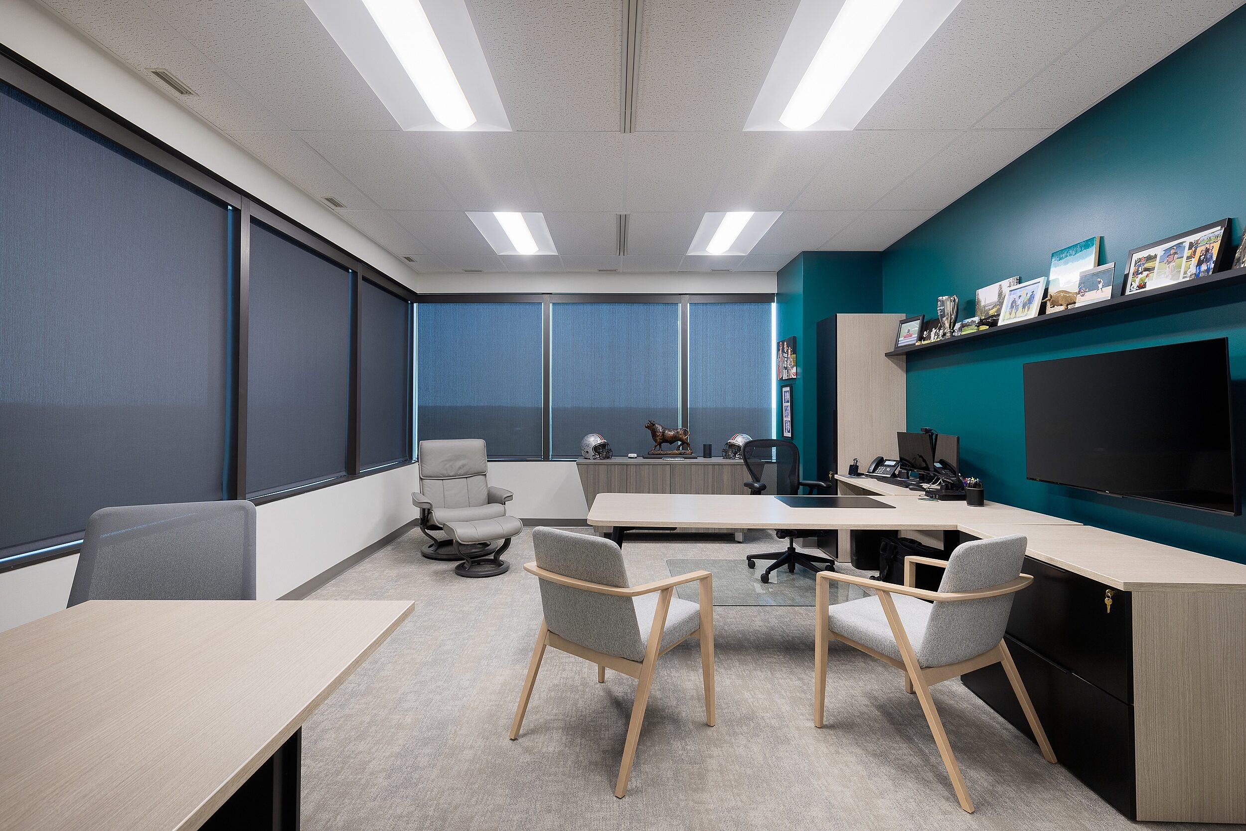 Large exec office with t-shaped desk with lots of storage and a wall mounted screen, two grey guest chairs, small conference table, lounge chair & ottoman