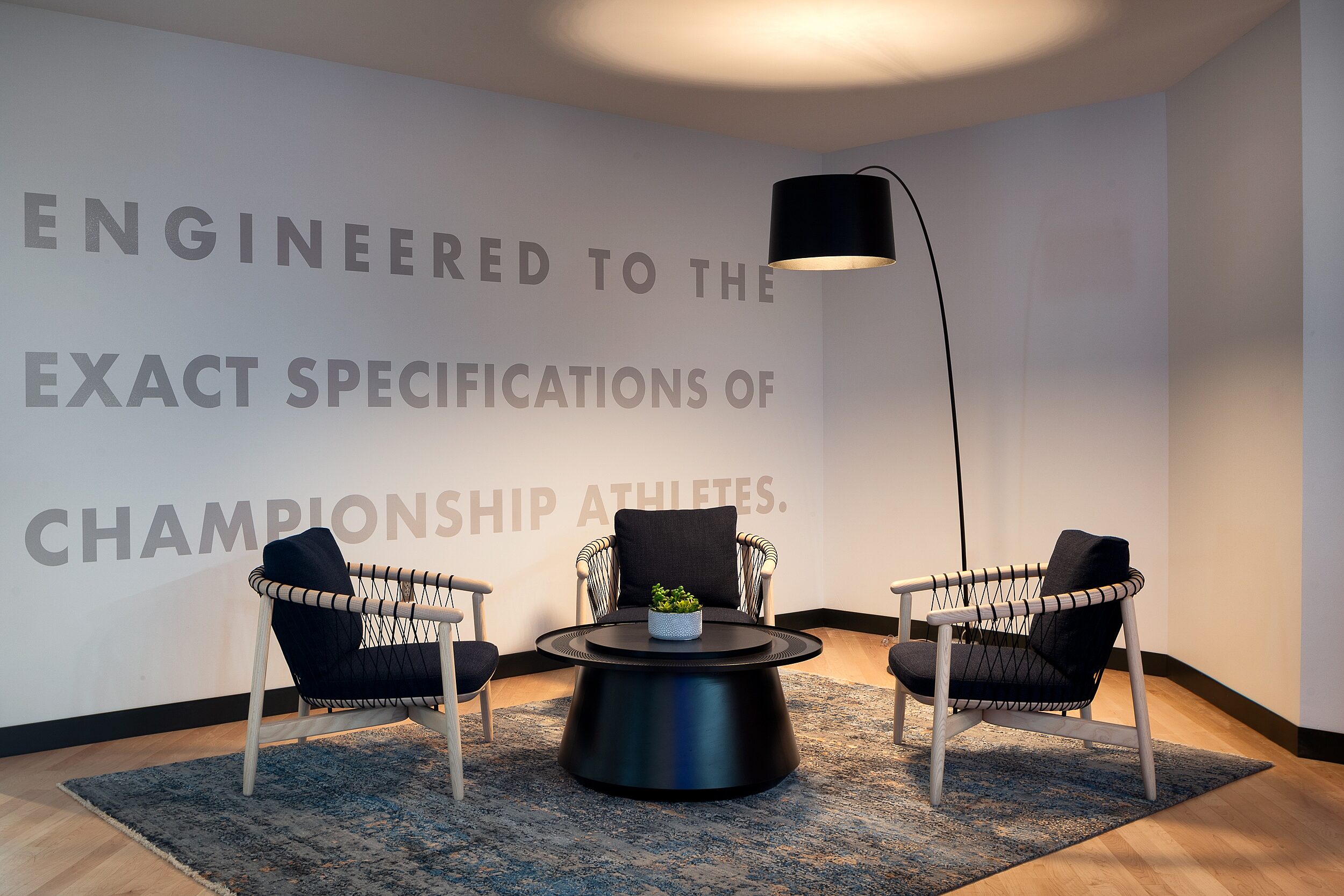 DRI seating area with three black/ash Geiger Crosshatch chairs around a black drum-styled coffee table and lamp with long extended arm. Wall mural behind