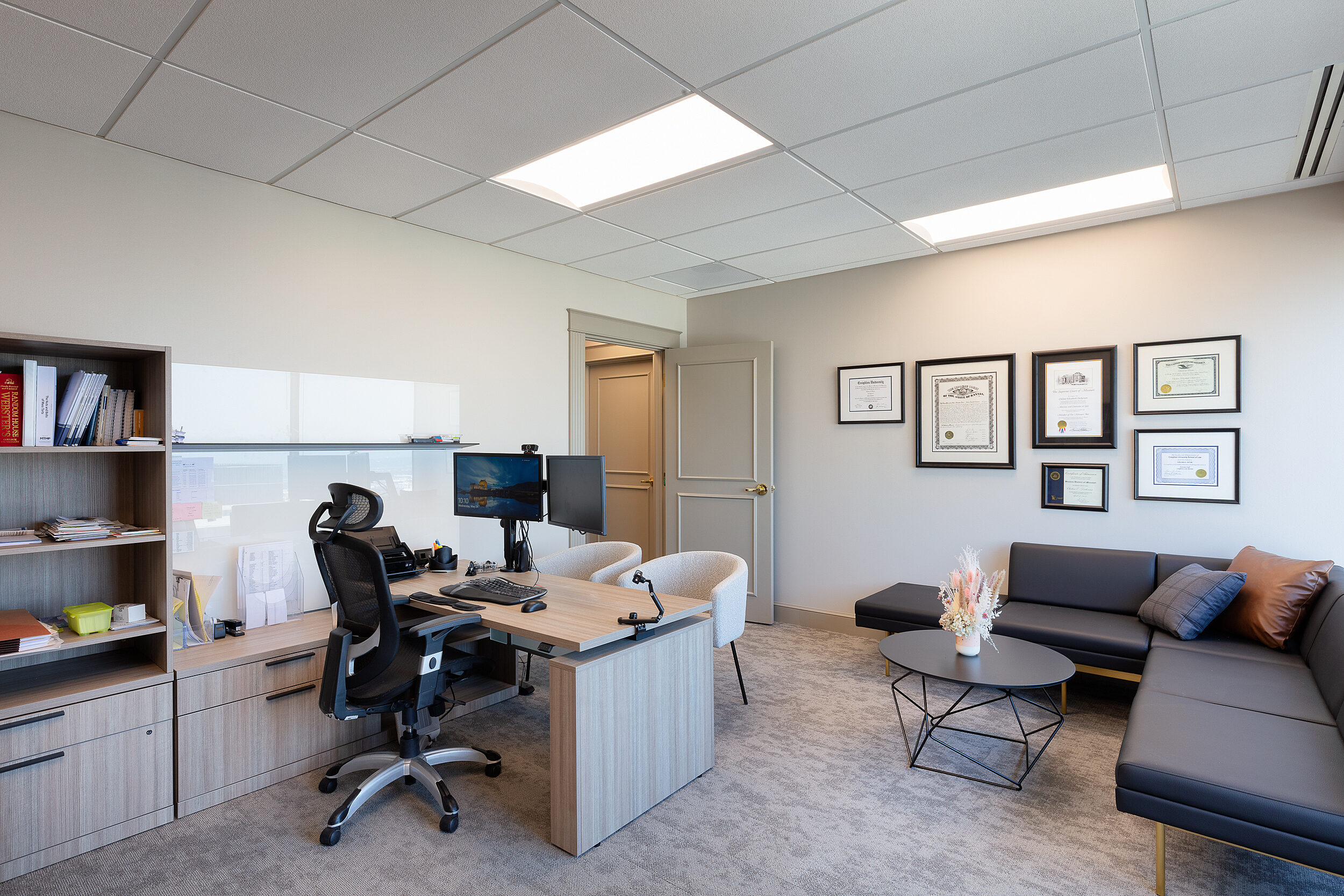 Executive law office with height adjustable desk with bookcases, office chair and grey L-shaped sofa with a matching coffee table in corner.