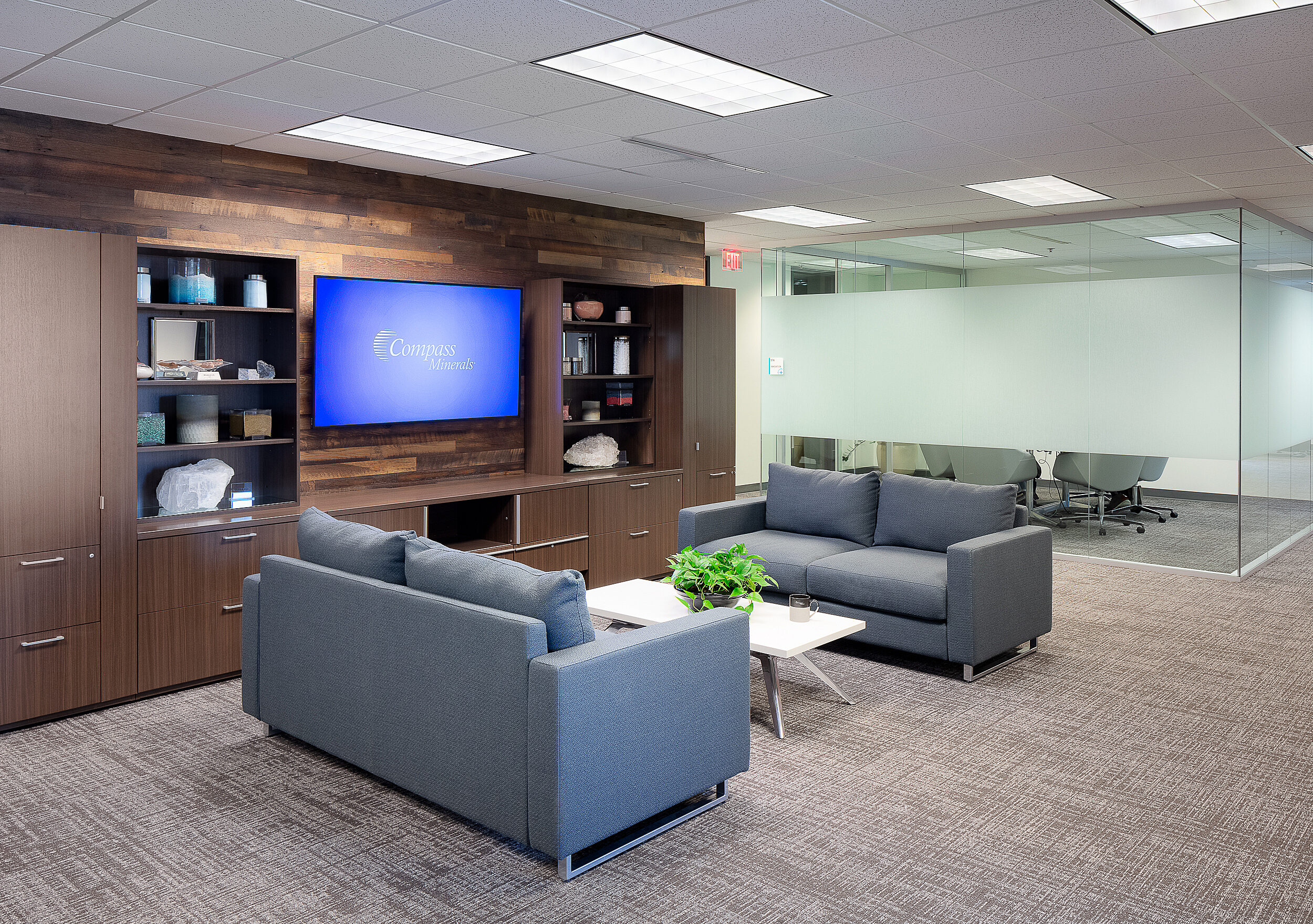 Compass Minerals Executive Reception area with two blue-grey couches and coffee table. Mounted tv on shelved wall featuring different types of salt