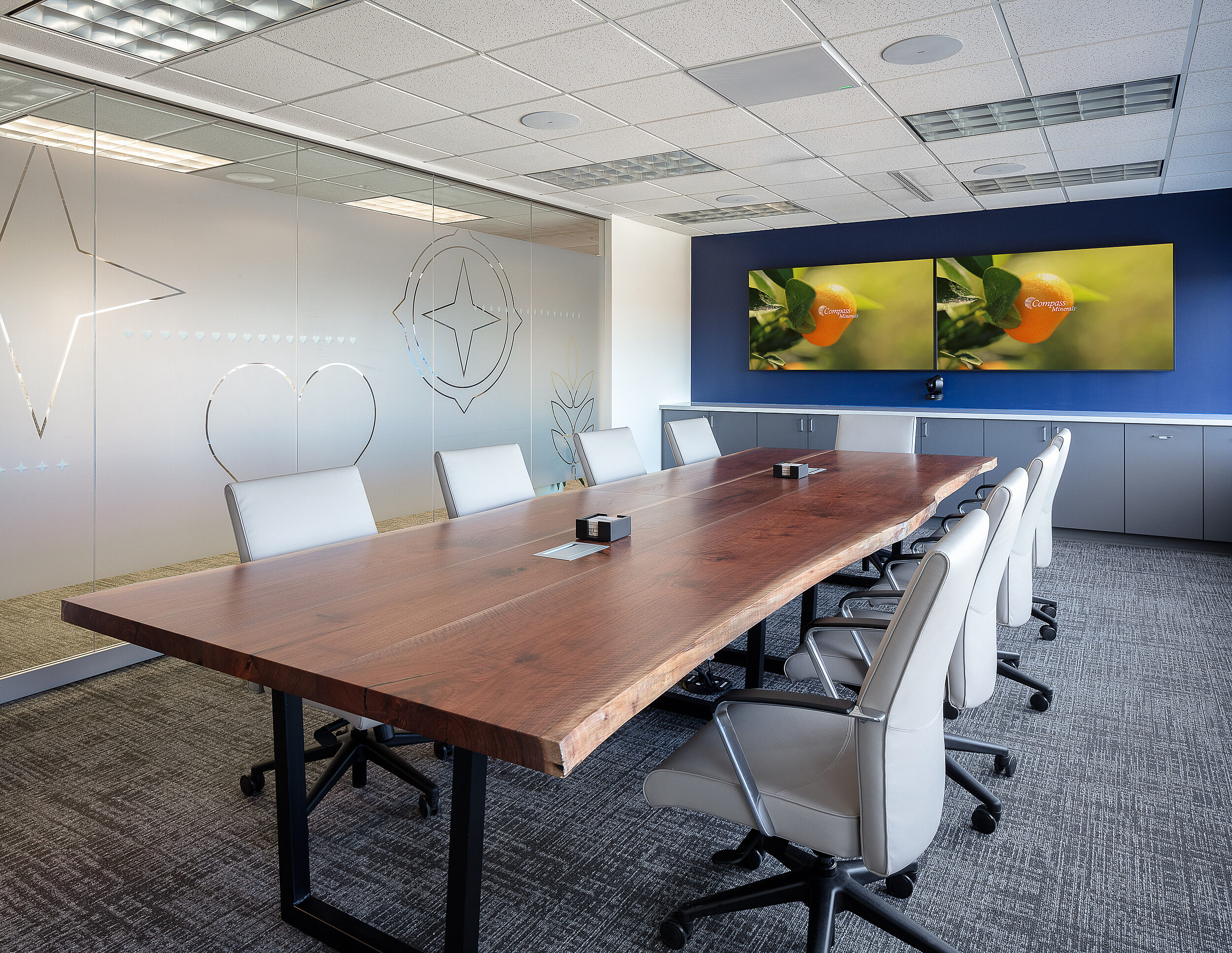 Compass Minerals - Conference room with custom live edge table and frosted glass wall with company icons. Double wide mounted screens with company images