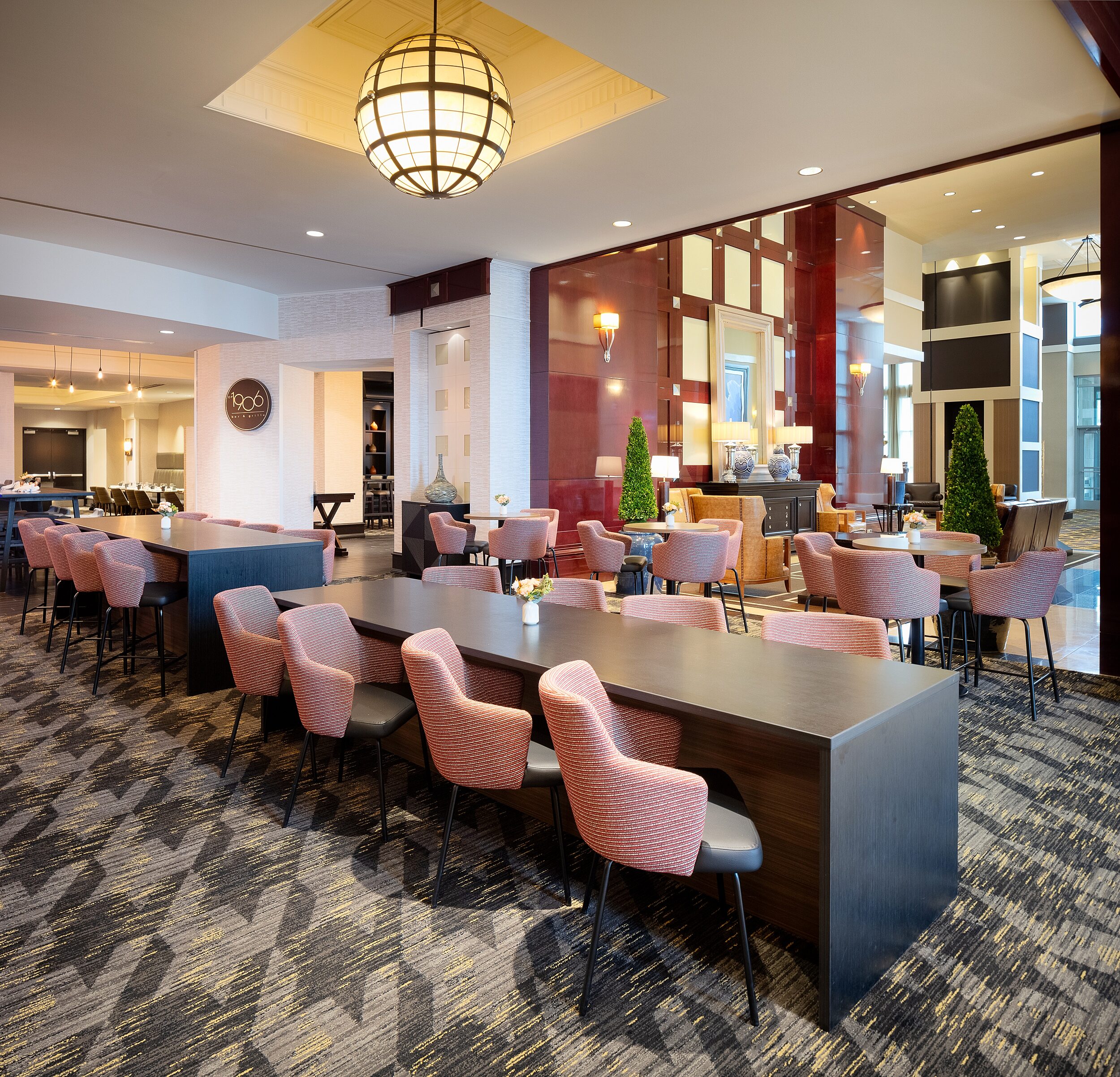 Short and tall, long black wooden bar tables. Chairs w/ red patterned upholstered backs and leather seats. Tall round bar tables and same chairs behind.