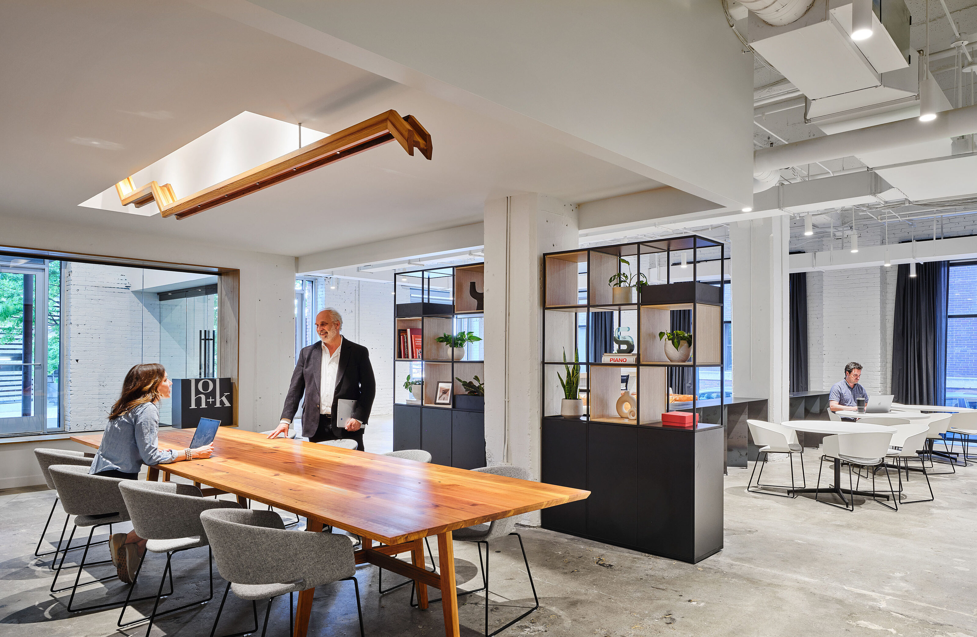 Small open meeting space with wooden table and grey chairs with tall, see-through shelving units sit off of main lobby area for impromptu, casual meetings