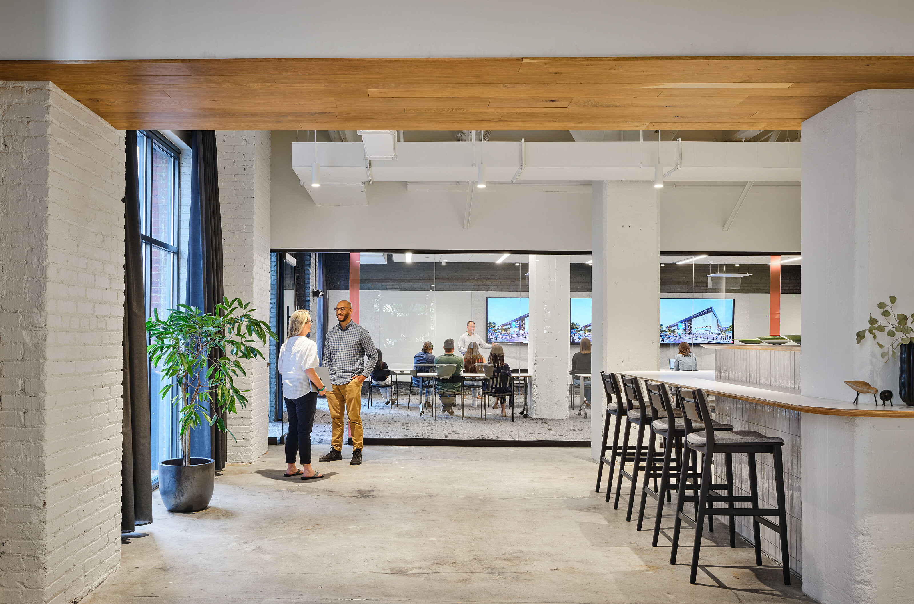 Counter-height seating with tall, black stools sit in open area off of breakroom. Man and woman chat while training session takes place in room behind them