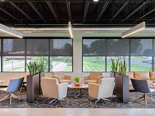 Long Watco seating area - mix of neugral/wood lounge chairs, couches, tables. Each area divided by planters with tall green plants. Grey patterned rug