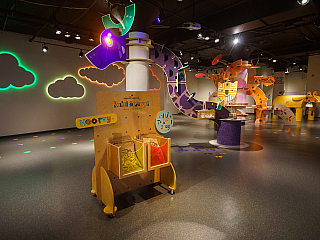 Hallmark Kaleidoscope logoed cart with a long, brigtly lit dragon display and lit up clouds on the walls. Several art stations can be seen throughout rom