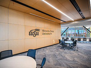 WSU Woolsey Hall-Wooden wall with college logo and round tables and rolling conference chairs give students several options to study and socialize.