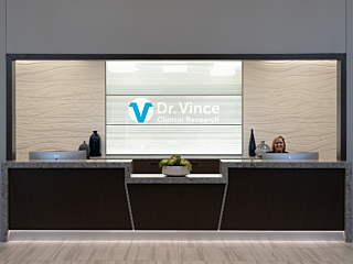 Dr. Vince Clinical Research reception area with logo on back wall, a smiling receptionist and a black counter with black marble waterfall trim