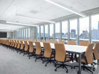 Large window-lined room with long conference table with 44+ camel leather high back chairs