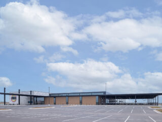 Exterior photo of The Hub building in Stillwater, OK, owned by the Tonkawa Tribe of Oklahoma, under blue sky with puffy white clouds.