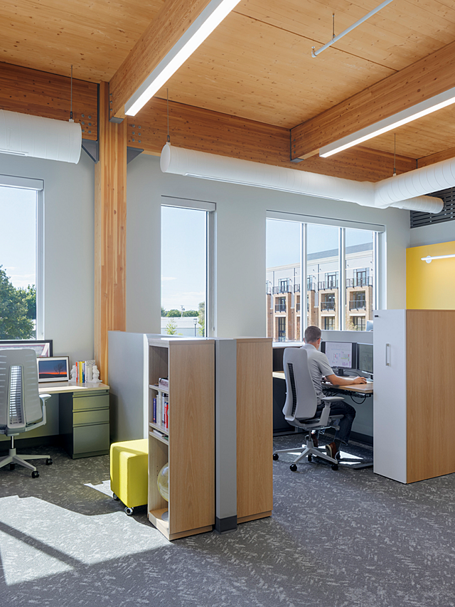 Hutton Construction-A male worker sits in grey office chair at height-adjustable desk. A custom storage lockers and bookcase unit sits next to each desk.