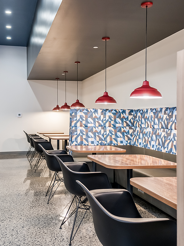 Schwan's company banquette seating with high back cushioning in blue/grey/yellow pattern. Wood cafe tables with alternate wide in molded black chairs.