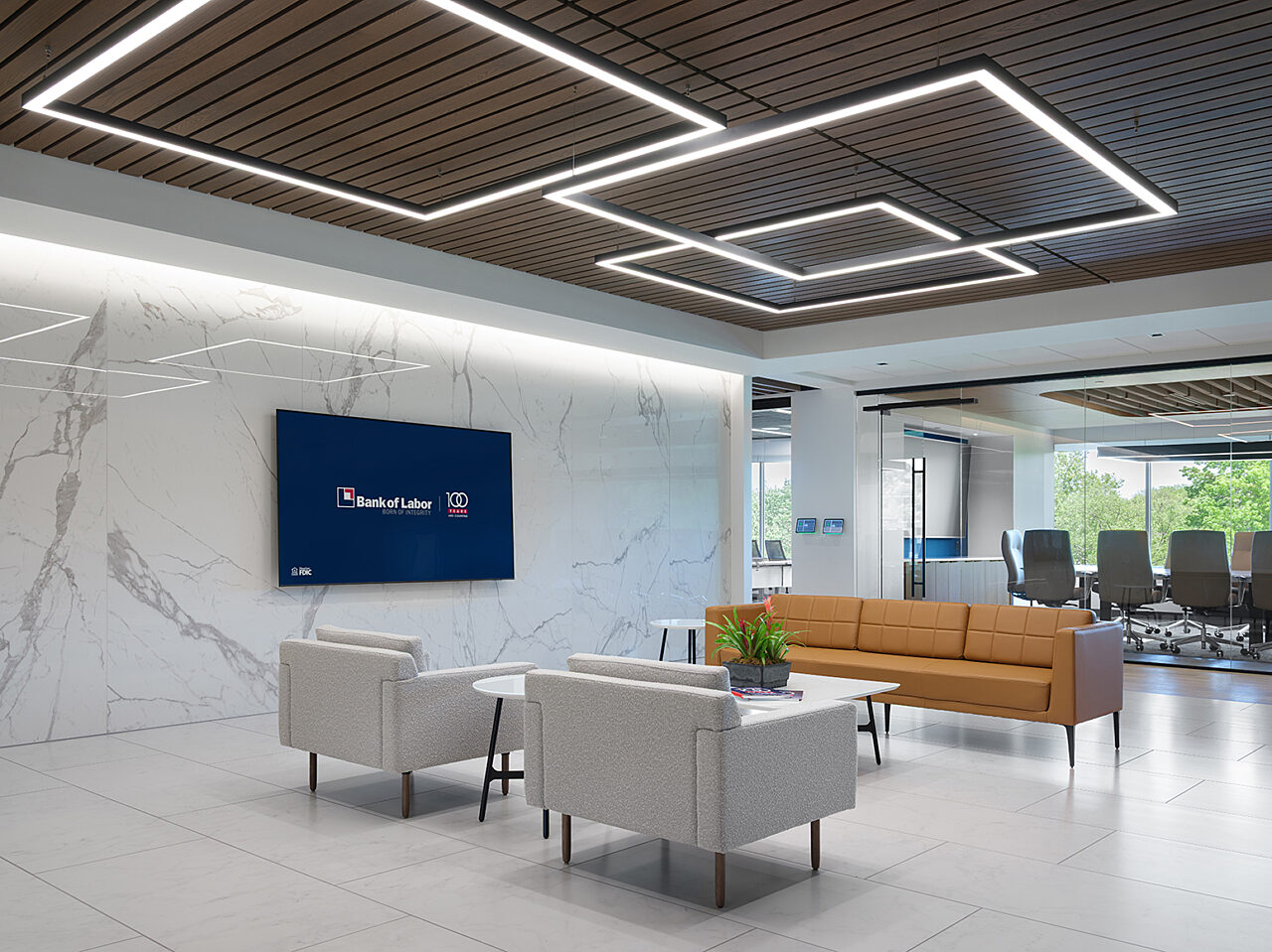 Reception seating area with white marble walls and mounted tv. Gold 3-seat couch with 2 facing lounge chairs in grey fabric, with coffee table with plant