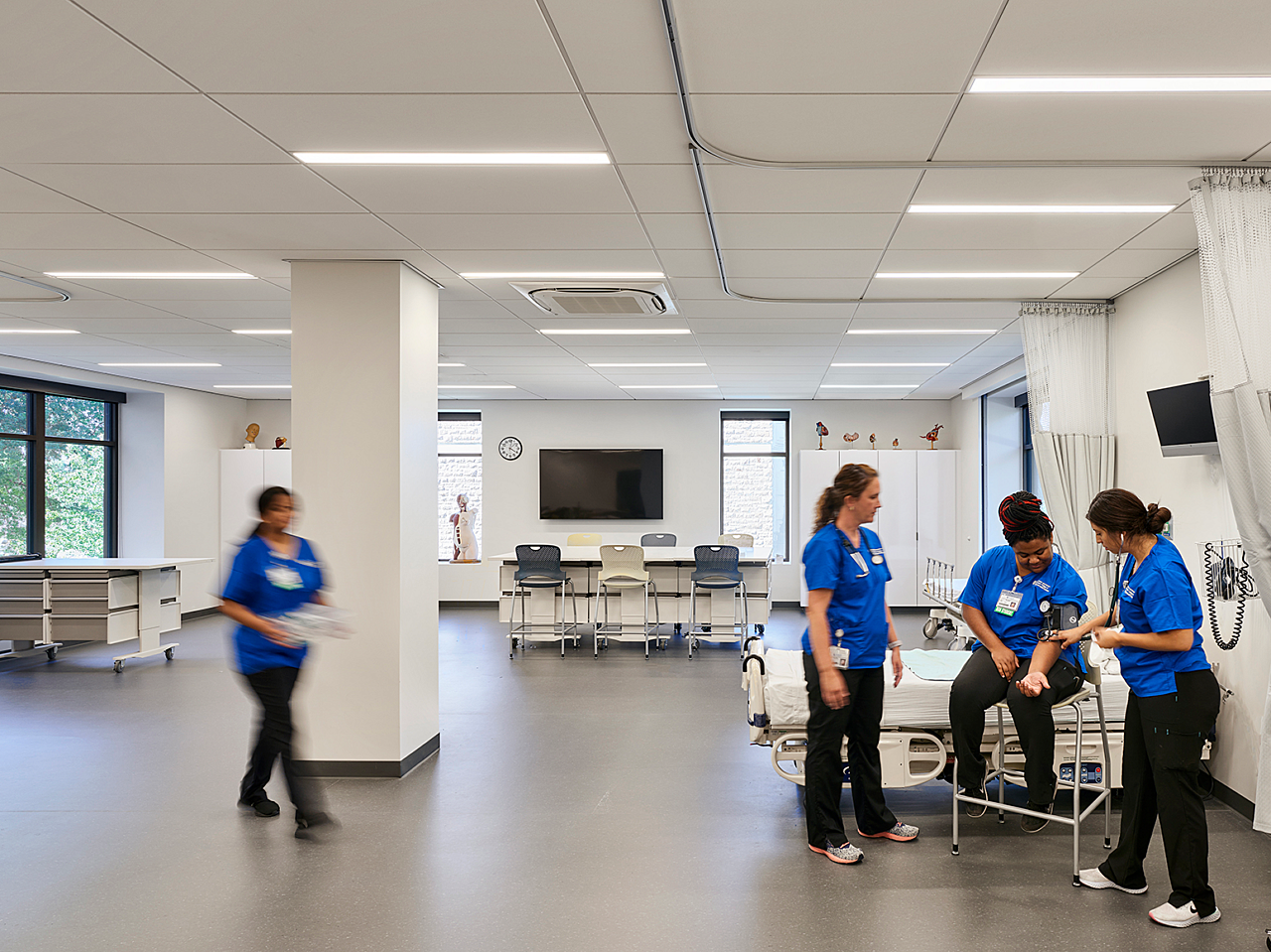 Rockhurst University's Sedgwick Hall nursing classroom with patient beds, carts and collaborative seating area. Students take each other's blood pressures