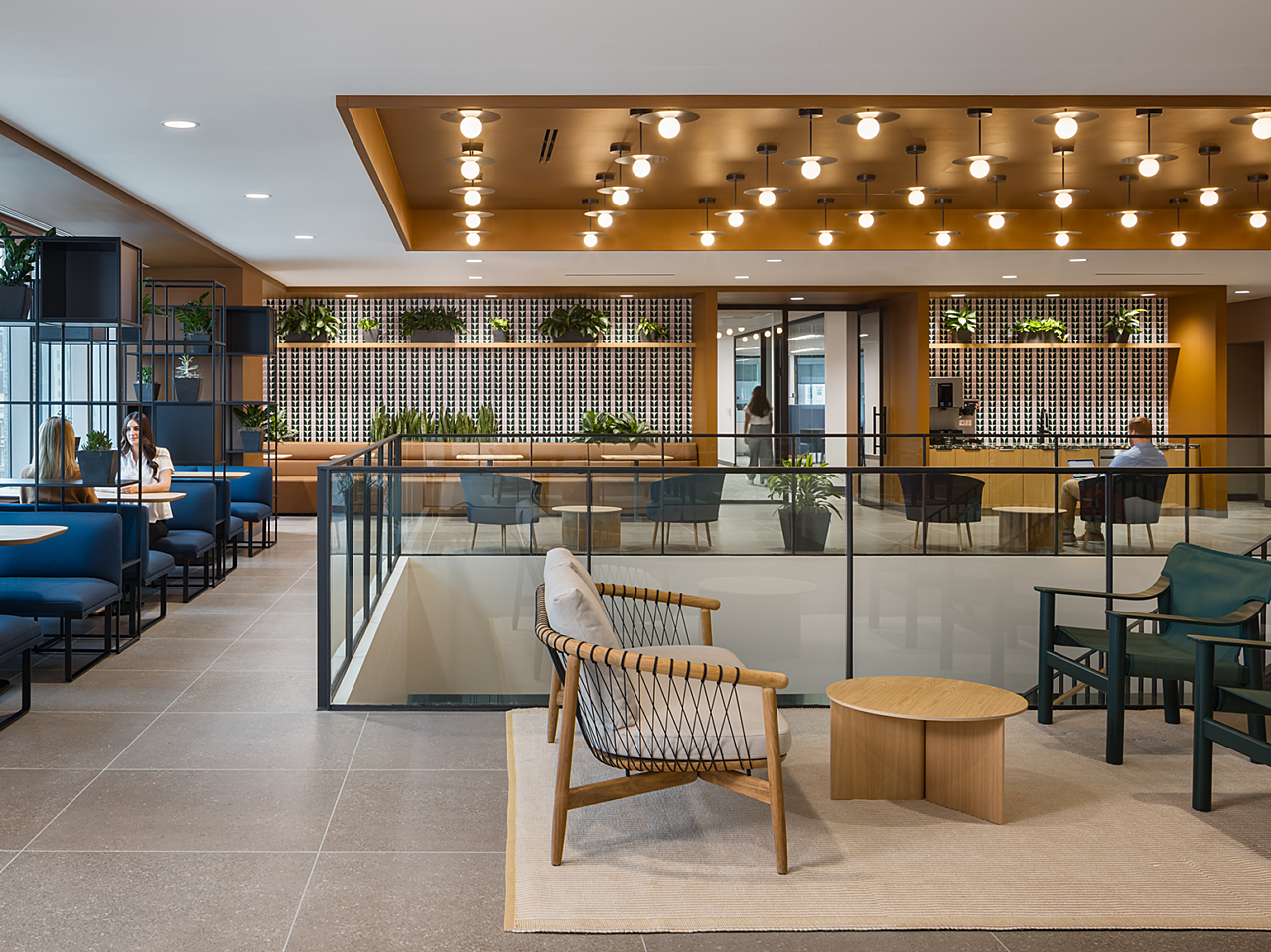 Lounge area with several seating options (booth, lounge and cafe) around center stairwell. Carmel and dark blue colors, plants, accent wallpaper in nooks
