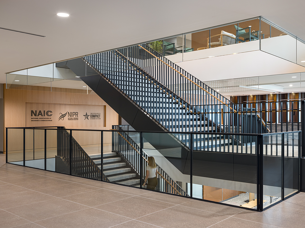 Black open stairwell between office floors with light railings. Wooden wall shows etched logos for NAIC, NIPR and another organization.